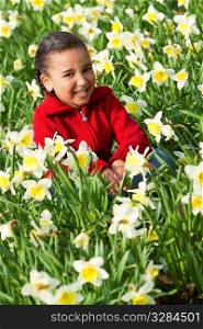 A beautiful young mixed race girl sitting and laughing in a field of daffodils