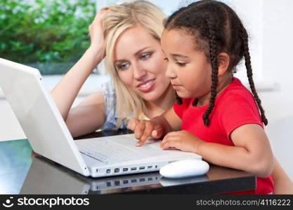 A beautiful young mother and her mixed race young daughter using a laptop at home in the kitchen.