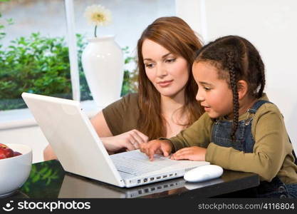 A beautiful young mother and her mixed race young daughter using a latop at home in the kitchen.