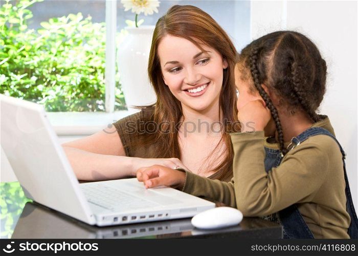 A beautiful young mother and her mixed race young daughter using a laptop computer at home in the kitchen.