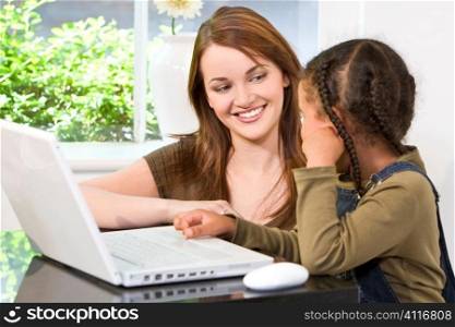 A beautiful young mother and her mixed race young daughter using a laptop computer at home in the kitchen.