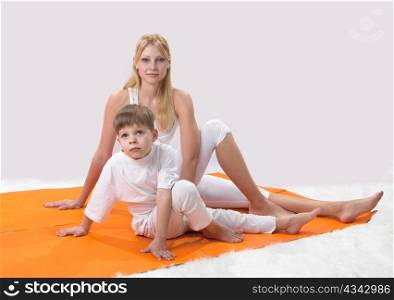 A beautiful young mother practices yoga with her son