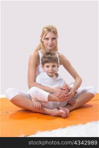 A beautiful young mother practices yoga with her son