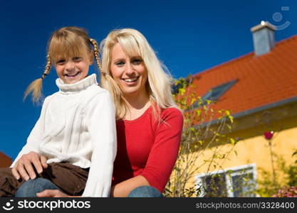 A beautiful young mother with her daughter under a blue sky in front of their home