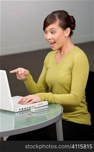 A beautiful young oriental woman using a laptop in her office looking happily surprised