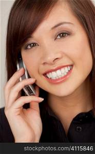 A beautiful young oriental woman with a wonderful smile chatting on her cell phone.