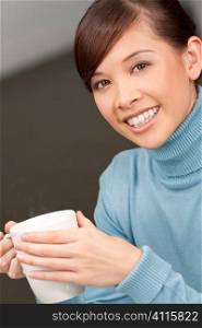 A beautiful young oriental woman with a wonderful toothy smile drinking a hot steaming drink from a white mug