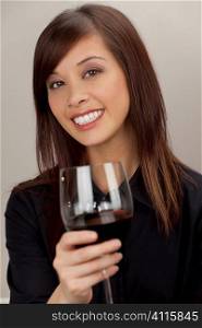 A beautiful young oriental woman with a wonderful toothy smile drinking raising a glass of red wine.