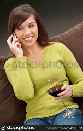 A beautiful young oriental woman with a wonderful toothy smile drinking red wine and chatting on her cell phone.