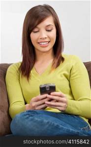 A beautiful young oriental woman with a wonderful toothy smile texting on her smartphone while sitting on a sofa