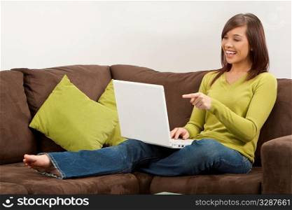 A beautiful young oriental woman with a wonderful toothy smile using a laptop on her sofa