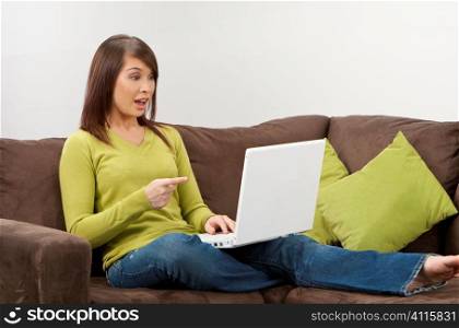 A beautiful young oriental woman with a wonderful toothy smile using a laptop on her sofa and looking surprised.