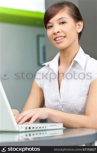 A beautiful young oriental woman with a wonderful toothy smile using a laptop
