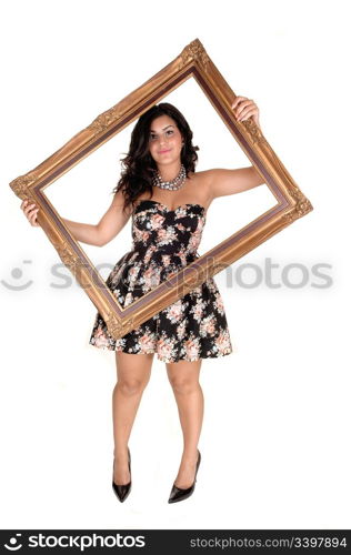 A beautiful young teenager in a nice dress holding up a golden old pictureframe, standing in the studio in high heels for white background.