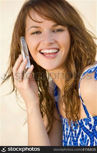 A beautiful young woman happily chatting on her mobile phone shot in golden summer sunshine at the beach