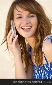 A beautiful young woman happily chatting on her mobile phone shot in golden summer sunshine at the beach