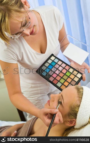 A beautiful young woman having the final touches applied to her make up by a beautician