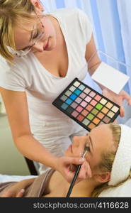 A beautiful young woman having the final touches applied to her make up by a beautician