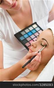 A beautiful young woman having the finishing touches applied to her make up by a beautician