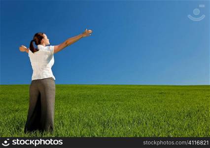 A beautiful young woman holding her arms out in praise or celebration standing in a green field and facing towards the light in a blue sky