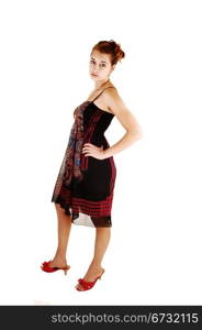 A beautiful young woman in a colorful black dress and red high heelsstanding for white background with her hands on her hips.