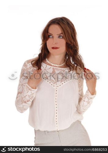 A beautiful young woman in a lace blouse and brunette hair standinglooking serious her hands holding hair, isolated for white background