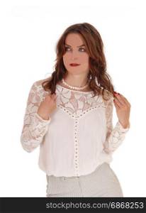 A beautiful young woman in a lace blouse and brunette hair standinglooking serious her hands holding hair, isolated for white background