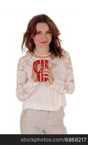 A beautiful young woman in a lace blouse standing isolated for white background holding a big red coffee mug and smiling.