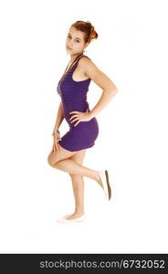 A beautiful young woman in a lilac dress, lifting up one leg,standing for white background with her hand on her hip.