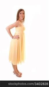 A beautiful young woman in a long yellow dress and high heels standingin profile in the studio, smiling into the camera, on white background.