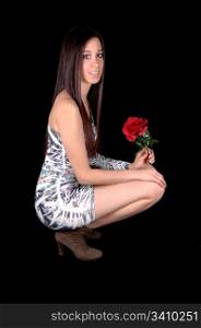 A beautiful young woman in a short tight dress, hocking on the floorin profile in the studio with a rose in her hand, for black background.