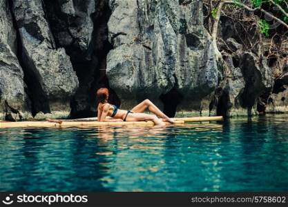 A beautiful young woman in a swimsuit is relaxing on a bamboo raft in a tropical lagoon