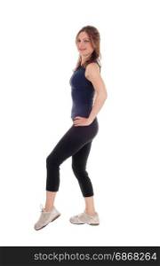 A beautiful young woman in an exercising outfit standing over whitebackground with her hands on her hips, in profile