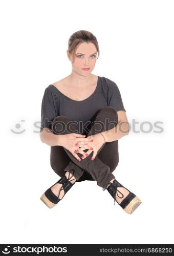 A beautiful young woman in jeans and brunette hair sitting with her legscrossed on the floor, looking serious, isolated for white background