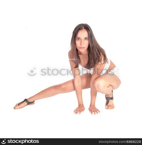 A beautiful young woman in shorts and white top and sandalscrouching on the floor, looking serious, isolated for white background