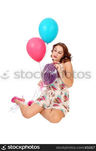 A beautiful young woman kneeling on the floor holding two balloons anda lollypop, isolated for white background.
