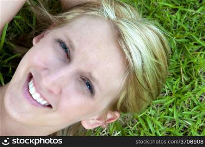 A beautiful young woman laying in a grassy yard. Sunset over a Lake