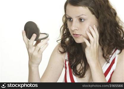 A beautiful young woman looks into a clasp mirror