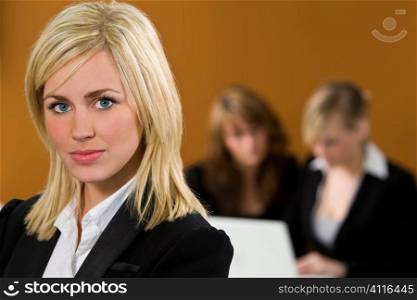A beautiful young woman manager with two female colleagues out of focus behind her working on a laptop