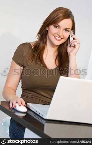 A beautiful young woman on her mobile phone while using her laptop computer