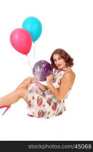 A beautiful young woman sitting on the floor holding two balloons anda lollypop, isolated for white background.