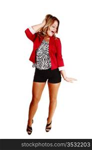 A beautiful young woman standing for white background in a red jacketblack shorts and heels, holding one hand on her head and laughing.