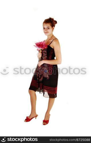 A beautiful young woman standing for white background in the studio,holding a pink water-lilly in her hand, in heels and a nice dress.