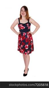 A beautiful young woman standing in black heels and a colorful printed dress with her hands on her hips, isolated for whitebackground