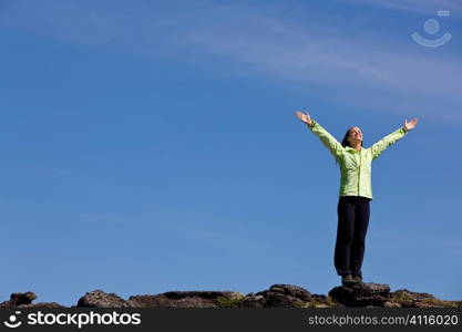 A beautiful young woman stands on the horizon arms raised celebrating reaching the top of a mountain.