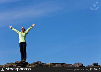 A beautiful young woman stands on the horizon arms raised celebrating reaching the top of a mountain.