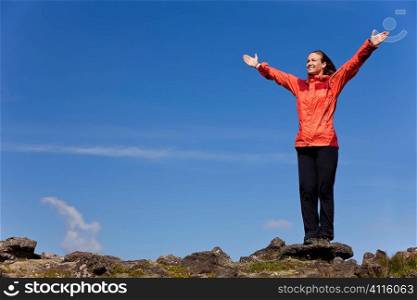 A beautiful young woman stands on the horizon arms raised celebrating reaching the top of a mountain.