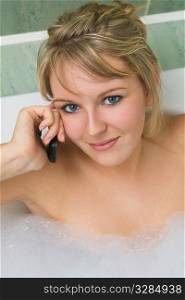 A beautiful young woman using her mobile phone while soaking in a bubble bath