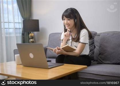 A beautiful young woman wearing headset is making video conference call via computer at home . Beautiful young woman wearing headset is making video conference call via computer at home