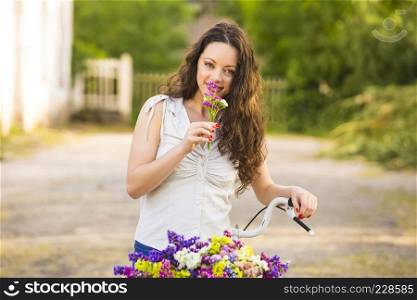 A beautiful young woman with her bicycle smelling wildflowers 